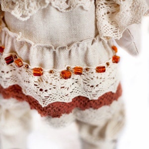 May include: A white linen dress with a lace overlay and a brown crocheted skirt. The dress is decorated with a row of amber beads.