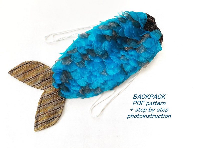 May include: A blue and brown fish-shaped backpack with a white drawstring. The backpack is made of fabric and has a scaly texture. The text "BACKPACK PDF pattern + step by step photoinstruction" is printed on a white background below the backpack.
