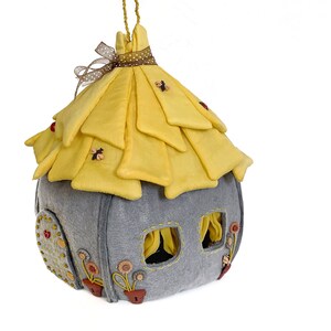 May include: A gray felt house with a yellow felt roof and a small door. The roof is decorated with small yellow bees and red ladybugs. The house has two windows with yellow curtains. The house is decorated with small yellow flowers and brown buttons.