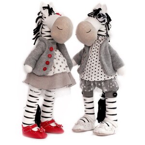 May include: Two plush zebra toys wearing dresses and jackets. One zebra has red shoes and the other has white shoes.