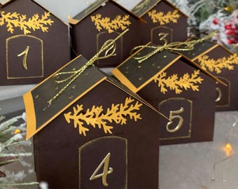 May include: A set of brown house-shaped boxes with gold detailing, numbered one to five. Each box features gold leaf patterns and is tied with gold ribbon. The roofs have an orange trim. Ideal for a festive occasion.