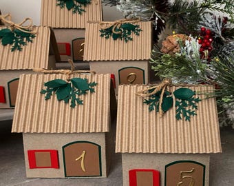 May include: Advent calendar in the shape of small houses made of corrugated cardboard. Each house has a brown door and red window, with a gold number. The roofs are decorated with green leaves and twine.