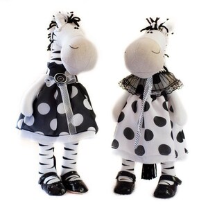 May include: Two plush zebra toys wearing black and white polka dot dresses. One zebra has a black bow and the other has a black lace collar.