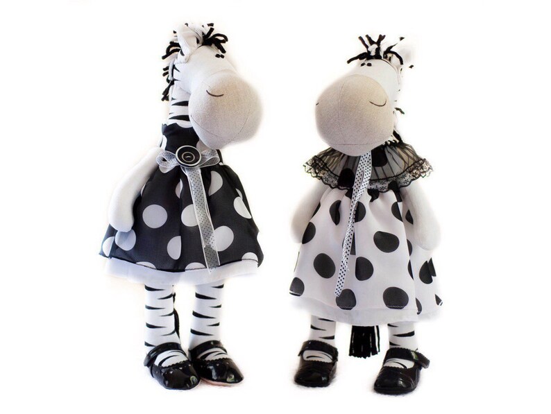 May include: Two plush zebra toys wearing black and white polka dot dresses. One zebra has a black bow and the other has a black lace collar.