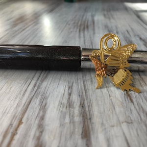 May include: A gold butterfly bookmark with a decorative swirl design. The bookmark is attached to a black and silver pen.