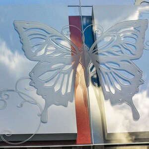 May include: A clear glass photo album with a butterfly design etched on the cover. The album is closed and sitting on a light blue box.