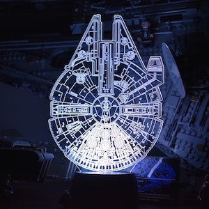 Peut inclure: Un modèle lumineux en acrylique blanc du vaisseau spatial Millennium Falcon de Star Wars. Le modèle est éclairé de l'intérieur, créant un contour lumineux du vaisseau.