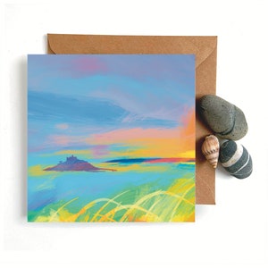 May include: A greeting card featuring a watercolour painting of a small island with a castle on it. The sky is a soft blue with pink and yellow clouds. The water is a light blue with green and yellow brushstrokes.