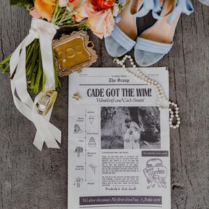 May include: A wedding still life featuring a bouquet of orange and pink flowers, a gold ring tray with rings, a newspaper with the headline "CADE GOT THE WIM!", light blue heels, and a pearl necklace. The newspaper has the text "JUST MARRIED".