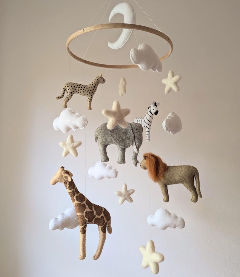 May include: A wooden baby mobile with a white felt moon, clouds, and stars. The mobile also features felt animal figures including a giraffe, lion, elephant, zebra, and cheetah.