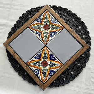 May include: A wooden frame with four tiles. Two tiles are gray and two tiles are decorated with colorful floral patterns. The frame is on a black crocheted doily.