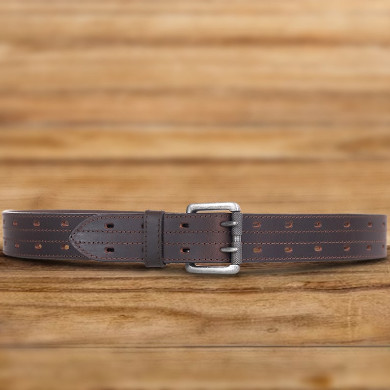 May include: A brown leather belt with a silver buckle and multiple rows of stitching. The belt has a series of evenly spaced holes for adjusting the fit.
