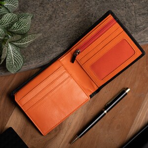 May include: A black leather wallet with an orange interior. The wallet has multiple card slots, a zippered compartment, and a clear ID window.