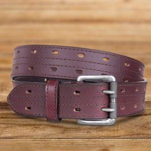 May include: A brown leather belt with a silver buckle. The belt has a stitched design and multiple rows of holes for adjusting the fit.
