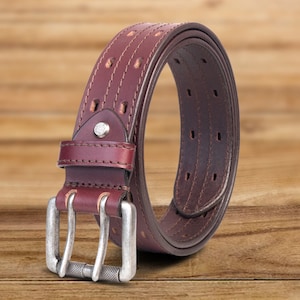 May include: A brown leather belt with a silver double prong buckle. The belt has a stitched design and multiple rows of holes for adjusting the fit.