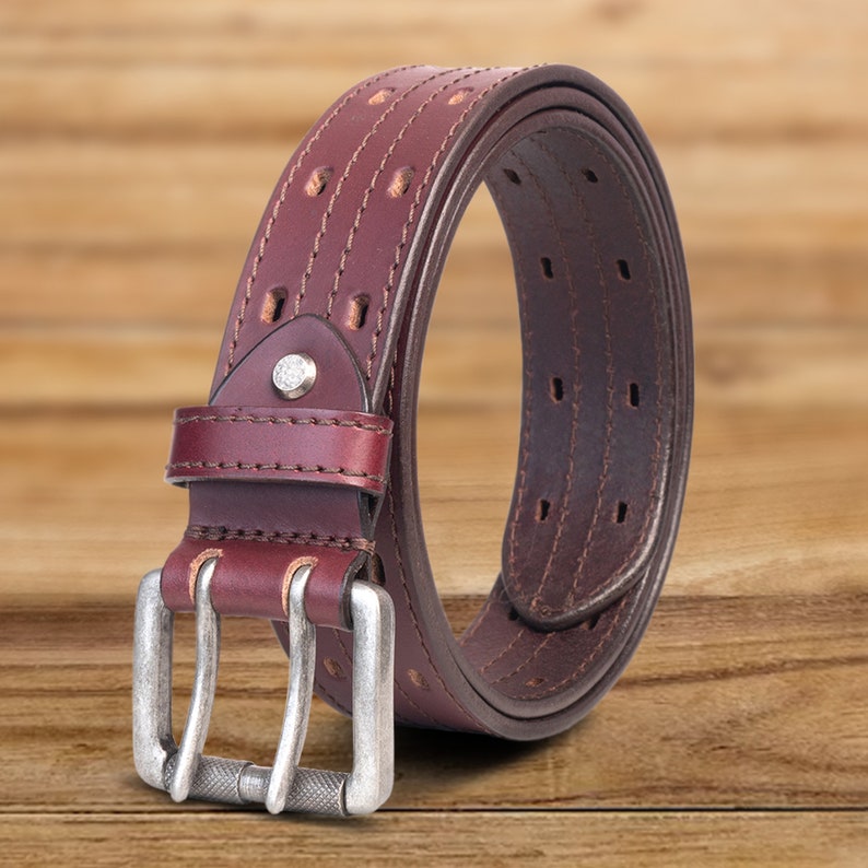 May include: A brown leather belt with a silver double prong buckle. The belt has a stitched design and multiple rows of holes for adjusting the fit.