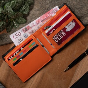 May include: A black leather wallet with an orange interior. The wallet is open and has several cards inside, including a Costa Coffee Club card. The wallet also has a zippered compartment.