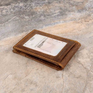 May include: A brown leather wallet with a clear plastic window for displaying an ID card. The wallet has yellow stitching around the edges.