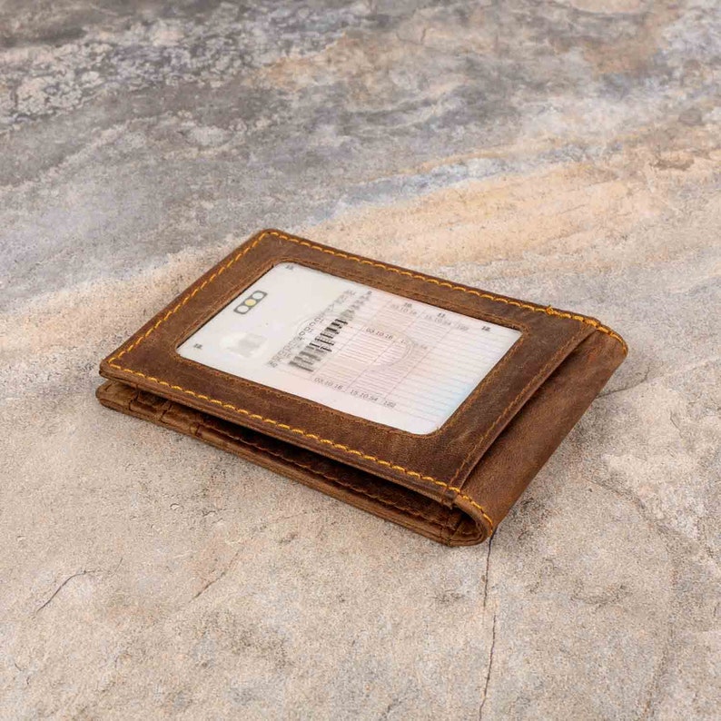 May include: A brown leather wallet with a clear plastic window for displaying an ID card. The wallet has yellow stitching around the edges.