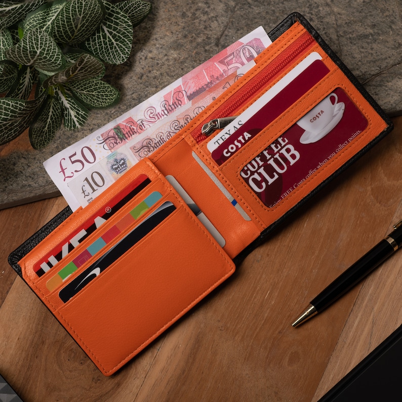 May include: A black leather wallet with an orange interior. The wallet is open and has several cards inside, including a Costa Coffee Club card. The wallet also has a zippered compartment.
