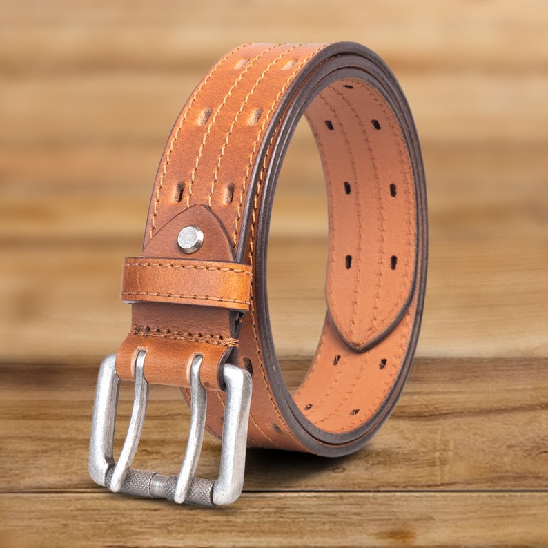 May include: A brown leather belt with a silver buckle. The belt has a stitched design and multiple holes for adjusting the size.