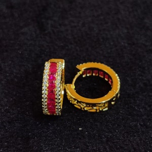 Può includere: Un paio di orecchini a cerchio dorati con una fila di pietre rosse e bianche.