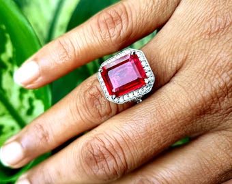 Peut inclure: Une bague en argent avec une grande pierre rouge de taille émeraude entourée de petites pierres claires.
