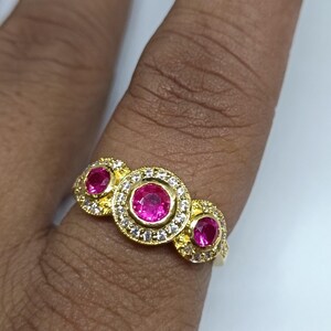 May include: A gold ring with three pink gemstones surrounded by smaller clear gemstones.