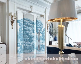 Puede incluir: Una cómoda blanca con tres cajones y un borde marrón oscuro se encuentra en una habitación con paredes blancas y una pantalla decorativa con un patrón floral azul y blanco. Una lámpara dorada con una pantalla blanca se encuentra en una mesa en el fondo.