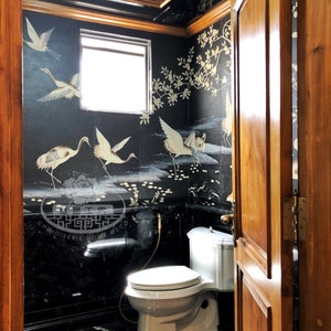 May include: A white toilet with a black and white tiled floor and a black and white wallpaper featuring a crane design. The text "Chinoiserie Home Deco" is visible on the wall.