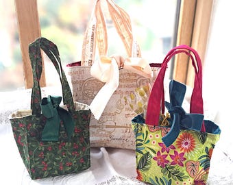 May include: Three small tote bags with different patterns and colors. One bag is green with red berries, another has musical notes, and the third is lime green with pink flowers. Each bag has a bow and handles.