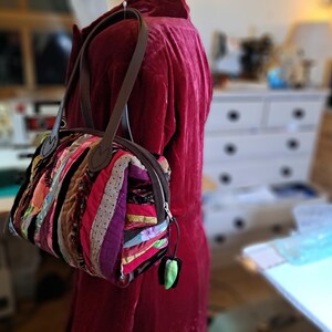 K&ouml;nnte beinhalten: Eine kleine, bunte Patchwork-Handtasche mit braunen Ledergriffen und einem Rei&szlig;verschluss. Die Tasche ist aus verschiedenen Stoffen gefertigt, darunter Streifen, Punkte und Blumenmuster.