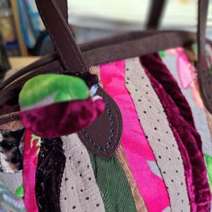 K&ouml;nnte beinhalten: Eine braune Ledertasche mit Patchwork-Design aus rosa, gr&uuml;nem, braunem und burgunderfarbenem Stoff. Die Tasche hat einen oberen Henkel und einen Klappenverschluss.