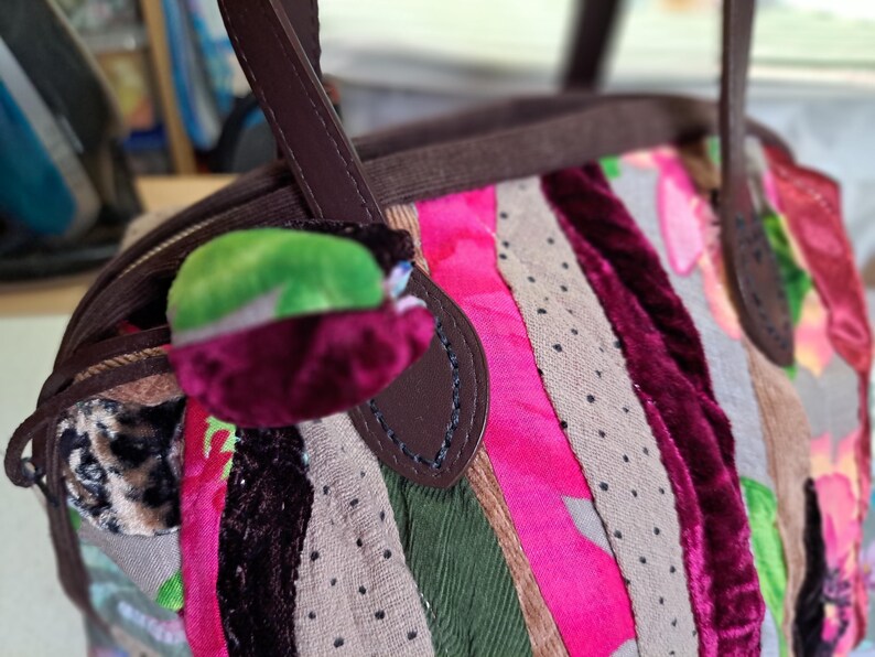 K&ouml;nnte beinhalten: Eine braune Ledertasche mit Patchwork-Design aus rosa, gr&uuml;nem, braunem und burgunderfarbenem Stoff. Die Tasche hat einen oberen Henkel und einen Klappenverschluss.