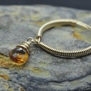 Könnte beinhalten: Ein Ring aus goldfarbenem Draht mit einem Anhänger aus bernsteinfarbenem Edelstein.