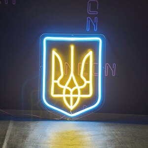 May include: A neon sign depicting the Ukrainian coat of arms, a yellow trident, inside a blue outline. The sign is mounted on a black wall.