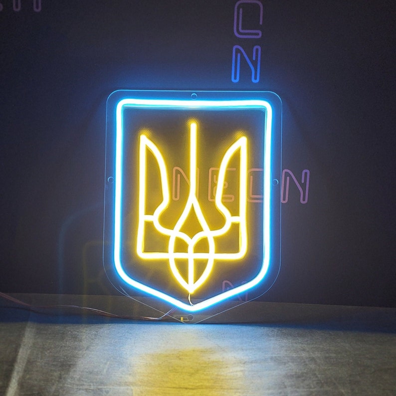 May include: A neon sign depicting the Ukrainian coat of arms, a yellow trident, inside a blue outline. The sign is mounted on a black wall.