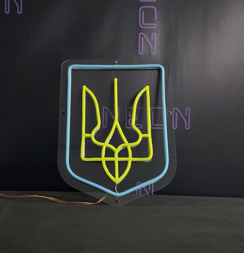 May include: A neon sign depicting the Ukrainian coat of arms, a yellow trident, inside a blue outline. The sign is mounted on a clear acrylic backing.