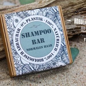 Könnte beinhalten: Eine braune Pappbox mit einem weißen Etikett, das mit einem floralen Muster und dem Text "Shampoo Bar - Normales Haar - 100% Natürlich - 100% Biologisch - 0% Plastik - Abbauar" verziert ist. Das Etikett enthält auch einen Kompass mit dem Text "Nordlicht Art - Estd 2017 - Plastic Free Products".
