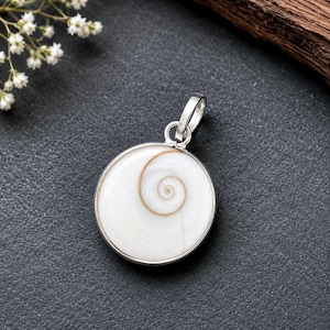Könnte beinhalten: Ein runder Anhänger mit einem weißen Shiva-Auge-Muschelstein, der ein natürliches braunes Spiralmuster aufweist und in eine silberfarbene Metallfassung mit einer kleinen Öse zum Aufhängen an einer Kette eingefasst ist.