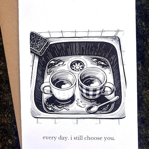Pode incluir: Ilustração a preto e branco de duas chávenas de café numa pia, com uma esponja e uma colher. O texto "every day. I still choose you." está impresso abaixo. O cartão está num envelope castanho.