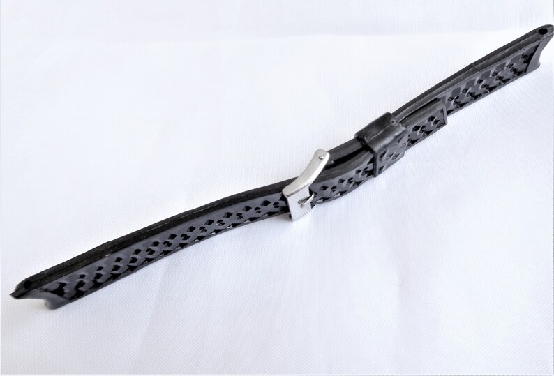 Puede incluir: Una correa de reloj de caucho negro con una hebilla de acero inoxidable. La correa tiene un dise&ntilde;o estampado.