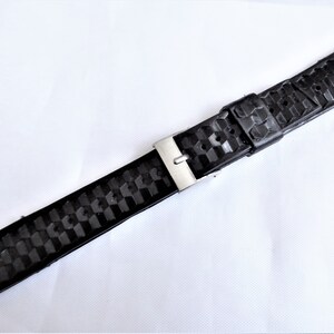 Puede incluir: Correa de reloj de caucho negro con hebilla plateada. La correa tiene un patr&oacute;n texturizado.