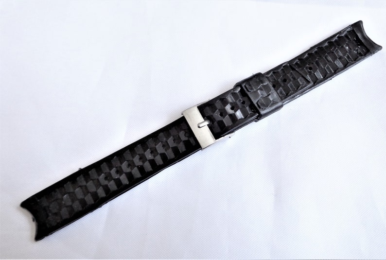 Puede incluir: Correa de reloj de caucho negro con hebilla plateada. La correa tiene un patr&oacute;n texturizado.