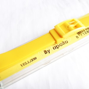 Könnte beinhalten: Ein leuchtend gelbes Uhrenarmband mit passender Schnalle. Das Armband ist mit "YELL/350" und "By apollo" gekennzeichnet. Das Armband ist auf einer gelben Rückseite mit Barcode und der Nummer "11.411" verpackt.