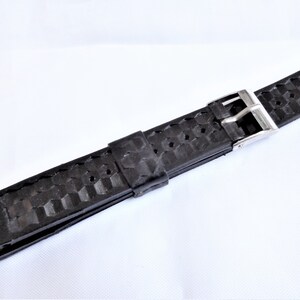 Puede incluir: Correa de reloj de caucho negro con hebilla plateada. La correa tiene un patr&oacute;n texturizado.