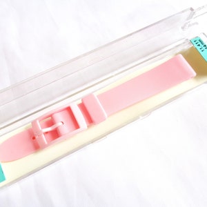 Könnte beinhalten: Ein rosafarbenes Silikon-Uhrenarmband mit einer silbernen Schließe. Das Armband befindet sich in einem durchsichtigen Plastikgehäuse mit einem Etikett mit der Aufschrift "11/411 350 14 mm".