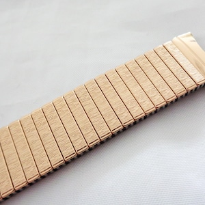 May include: A gold-toned metal watch band with a brushed finish. The band is made of many small, linked pieces.