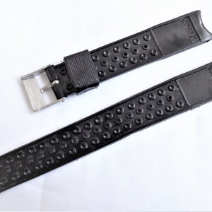 Puede incluir: Correa de reloj de caucho negro con hebilla plateada. La correa tiene una superficie texturizada con peque&ntilde;os c&iacute;rculos. La hebilla tiene el texto "SEIKO" en ella.