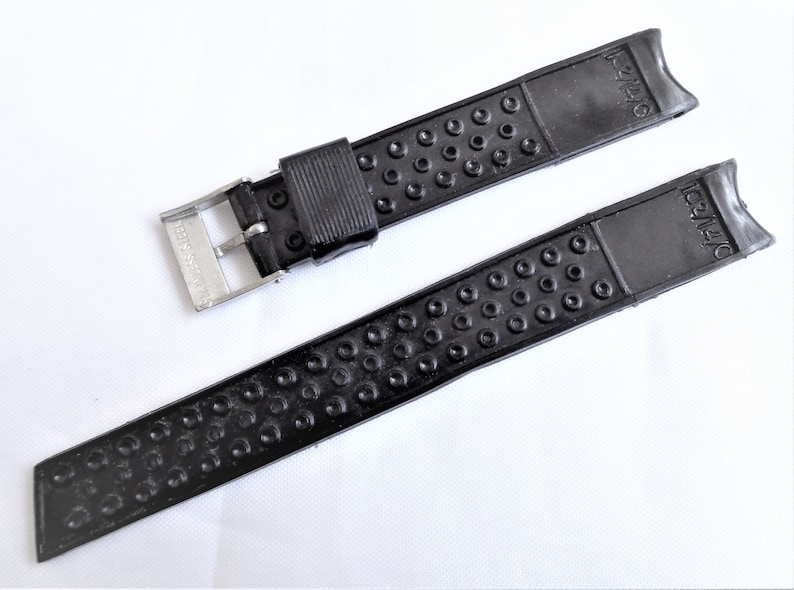 Puede incluir: Correa de reloj de caucho negro con hebilla plateada. La correa tiene una superficie texturizada con peque&ntilde;os c&iacute;rculos. La hebilla tiene el texto "SEIKO" en ella.